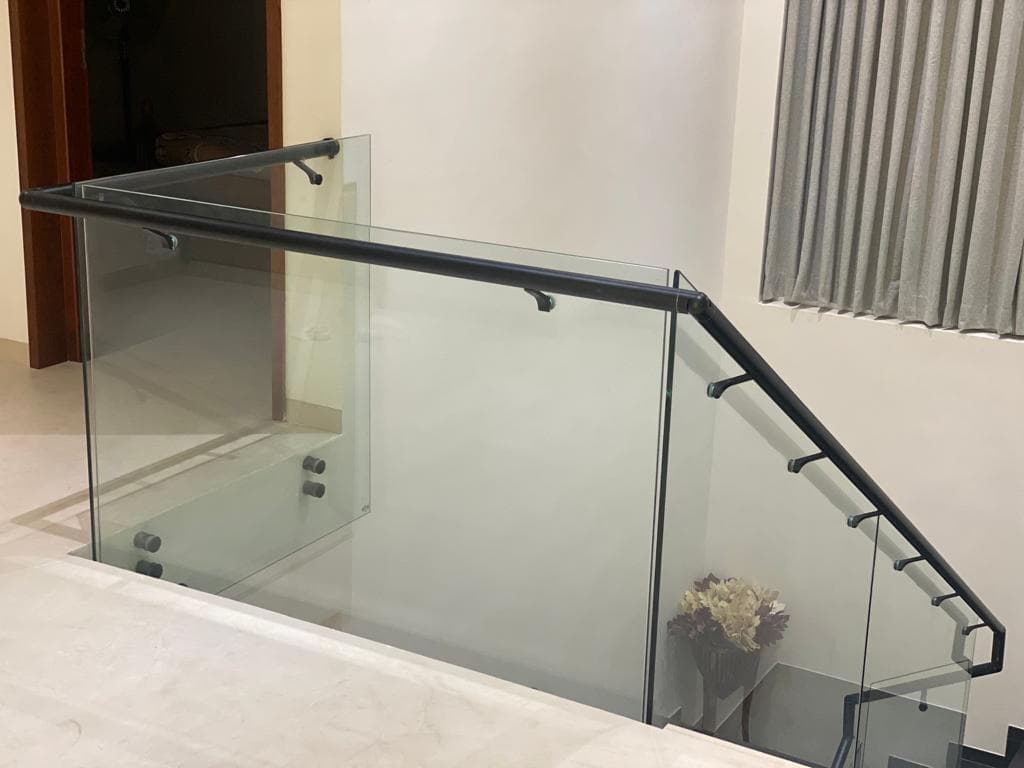 Glass railing with a dark handrail beside an interior staircase
